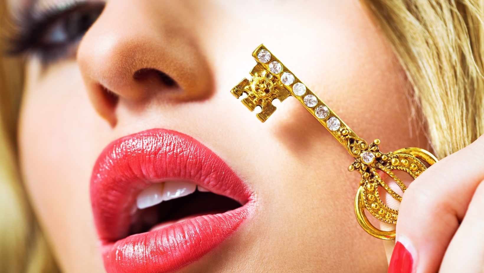 Ausschnitt eines weiblichen Gesichts. Die Lippen, rot-rosa geschminkt und leicht geöffnet. Ein goldener Schlüssel liegt leicht an der Wange an.
